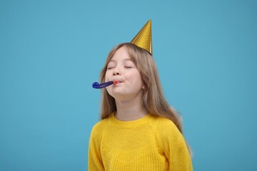 Cute little girl in party hat with blower on light blue background