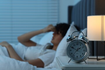Young woman suffering from headache in bed at night, focus on alarm clock