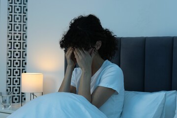 Young woman suffering from headache in bed at night