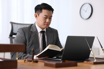Notary working with laptop and book at wooden table in office