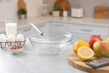 Metal whisk, bowl, grater and different products on gray marble table in kitchen