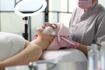 Obraz na płótnie Canvas Cosmetologist applying mask on woman's face in clinic, closeup