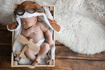 Cute newborn baby wearing aviator hat with toy sleeping in wooden crate, top view. Space for text