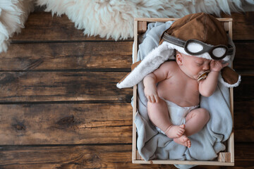 Cute newborn baby in aviator hat sleeping on wooden background, top view. Space for text