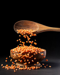 In the foreground, cascade of red lentils in the wooden bowl