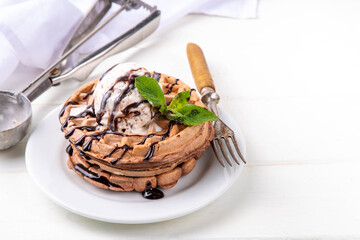 Stack of chocolate belgian waffles with ice cream and chocolate topping. Breakfast waffles with gelato, chocolate sauce drizzles and mint