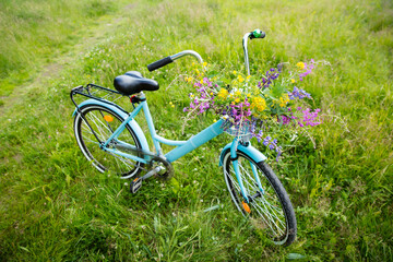 Bike with a basket of wild flowers on a meadow. Sunny summer day, rays of light, rural background. Summer vacation concept.