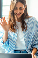 Happy young attractive woman in glasses looking at laptop screen, waving hands, holding video call...