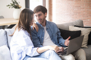 Couple in blue denim casual clothes using together a laptop sitting comfortable on the sofa at home...