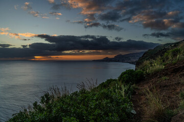 Fototapeta na wymiar A serene view of a Village rocky coast , under a dusk sky with fluffy clouds Colorful sunset at Caniço, Madeira island, Portugal