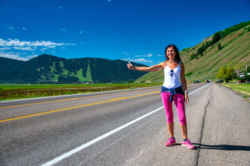Obraz premium A woman hitchhikes on a Wyoming road in the summertime.