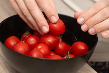 Cherry Tomatoes in a bowl in female hands. Hands cradling a black bowl filled with bright red...