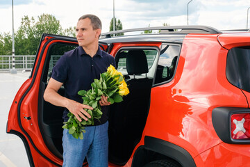 A man with flowers in his hands stands near a car - 761601621