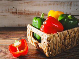 A basket full of colorful peppers on a wooden surface.