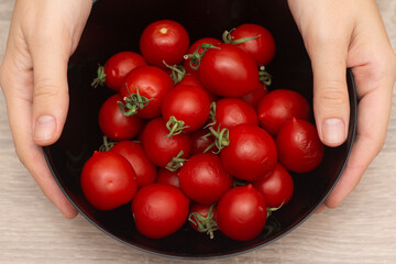 Cherry Tomatoes in a bowl in female hands. Hands cradling a black bowl filled with bright red...
