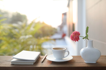 ceramic coffee cup and a white vase of rose flowers and notebooks