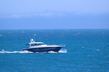 A side view of a beautiful motorboat with blue details sailing across the sea, making waves in the...