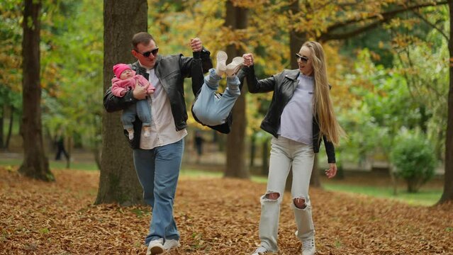 Joyful Family Moment With Playful Jump in Autumn Park. A playful leap by a young boy holding his parents' hands amidst the autumn leaves brings joy to a family walk. Concept Autumn Family Fun