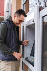 Fototapeta premium A one young man withdrawing money on ATM with credit card in the city