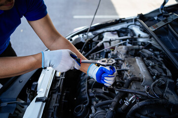 Fototapeta premium A man is working on a car engine. He is wearing blue gloves and a blue shirt. The car is silver and has a hood up