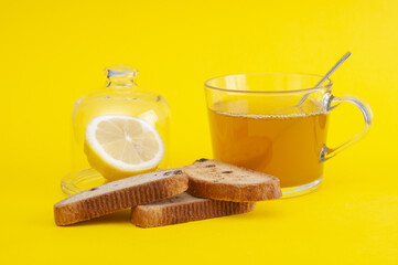 Cup of tea with rusks and lemon on yellow background