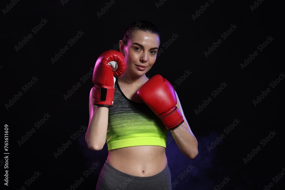 Poster Portrait of beautiful woman wearing boxing gloves in color lights on black background