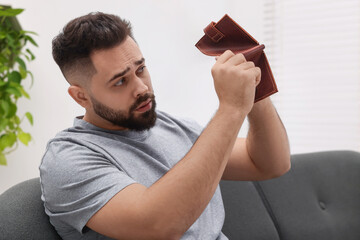 Upset man with empty wallet on sofa indoors