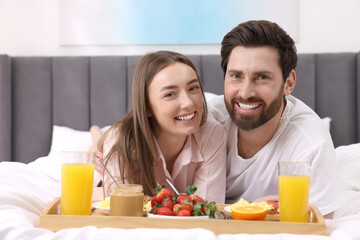 Obraz na płótnie Canvas Family portrait of happy couple with tray of tasty breakfast on bed at home