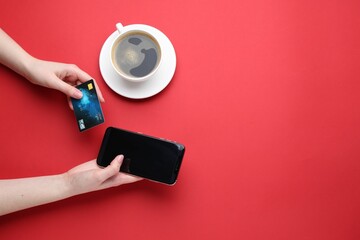 Online payment. Woman with smartphone, credit card and coffee on red background, top view. Space...