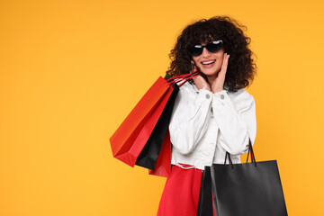 Happy young woman with shopping bags and stylish sunglasses on yellow background. Space for text