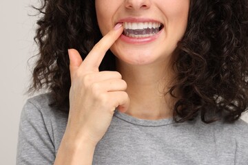 Young woman applying whitening strip on her teeth against light grey background, closeup