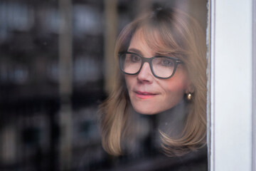 Headshot of an attractive mid aged woman standing behind the glass window and daydreaming