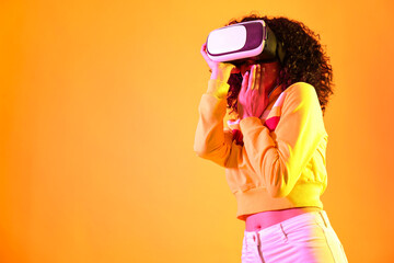 Beautiful young woman with virtual reality headset on color background in neon lights