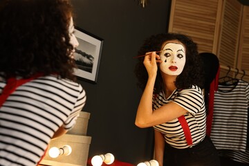 Young woman applying mime makeup near mirror indoors