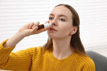 Medical drops. Young woman using nasal spray indoors