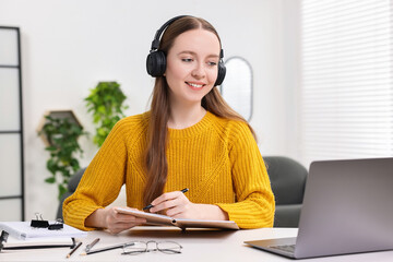 E-learning. Young woman taking notes during online lesson at white table indoors