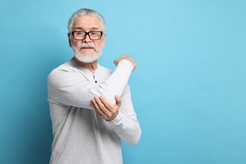 Arthritis symptoms. Man suffering from pain in elbow on light blue background, space for text