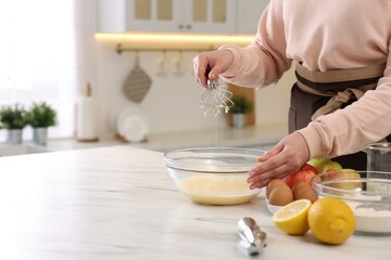 Woman whisking eggs in bowl at light marble table indoors, closeup. Space for text
