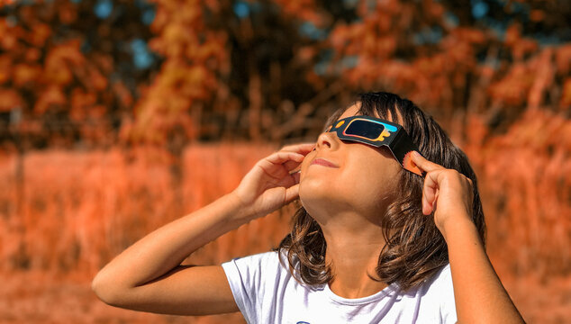 Fototapeta A young girl looking at the sun during a solar eclipse on a country park, family outdoor activity