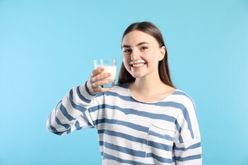 Happy woman with milk mustache holding glass of tasty dairy drink on light blue background