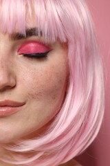 Beautiful woman with bright makeup and fake freckles on pink background, closeup