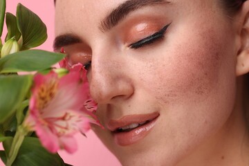 Beautiful woman with fake freckles and flower on pink background, closeup