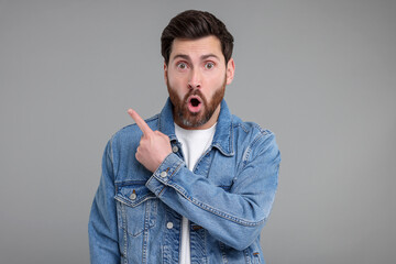 Surprised man pointing at something on grey background