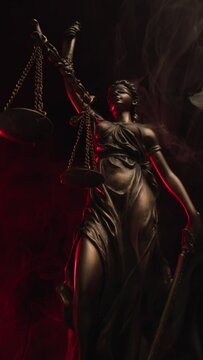 female marble statue holding sword and balance in hand on dark background with smoke effect