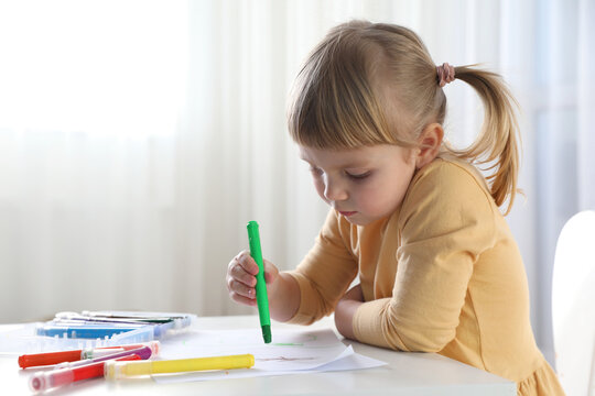 Cute little girl drawing with marker at white table indoors. Child`s art
