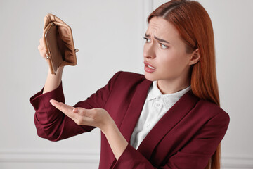 Upset woman with empty wallet near white wall