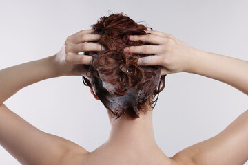 Naklejka premium Young woman washing her hair with shampoo on light grey background, back view
