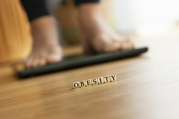 Obesity word with woman feet on a weight scale in background suggesting fighting with kilograms concept - 761628276