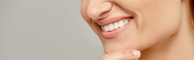 cropped banner of woman with healthy smile touching radiant skin on grey background, close up