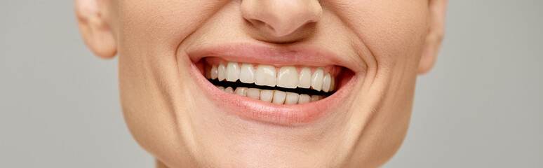 cropped banner of happy woman exuding joyful and healthy smile on grey background, white teeth